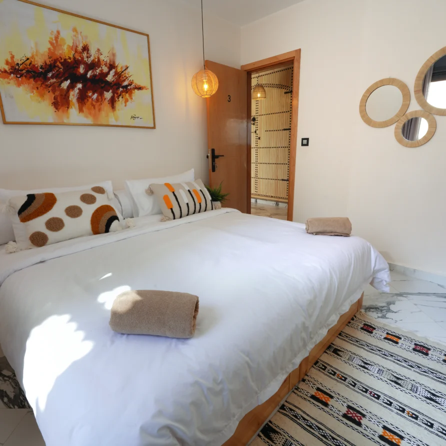 Extra-long double bed with white linens and bedside lights in the Deluxe Double Room, Residence Imsouane Surf Camp.