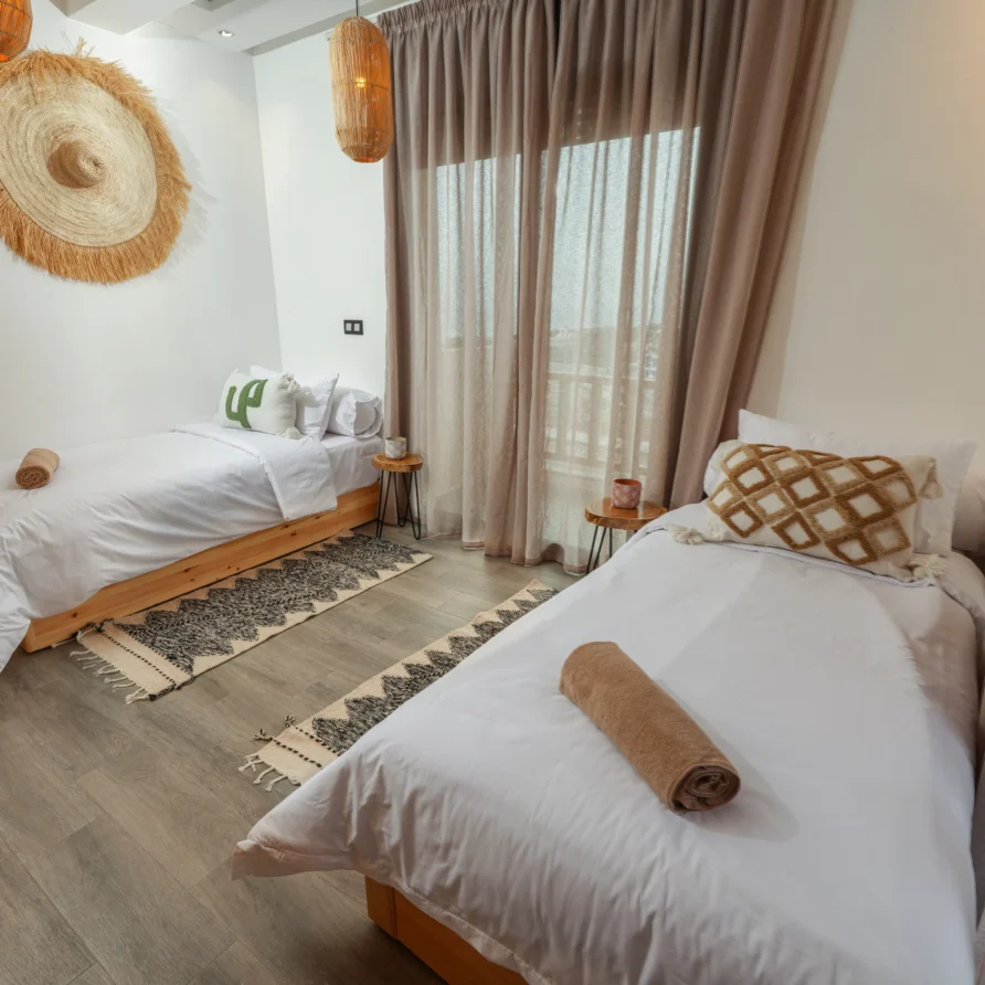 Two single beds with boho décor, rugs and balcony curtains in a mountain-view room